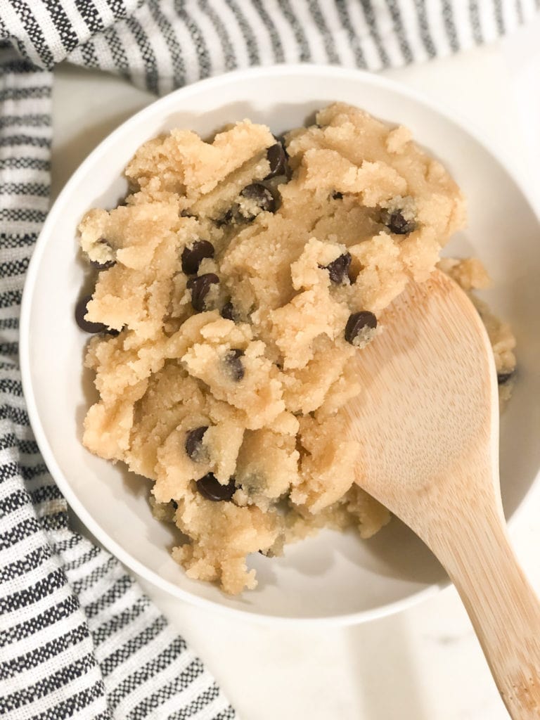 Close up of edible chocolate chip cookie dough in white bowl with wooden spoon