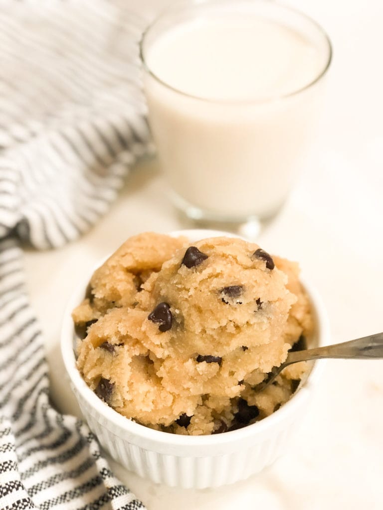 Close up of edible chocolate chip cookie dough in white bowl with a glass of milk