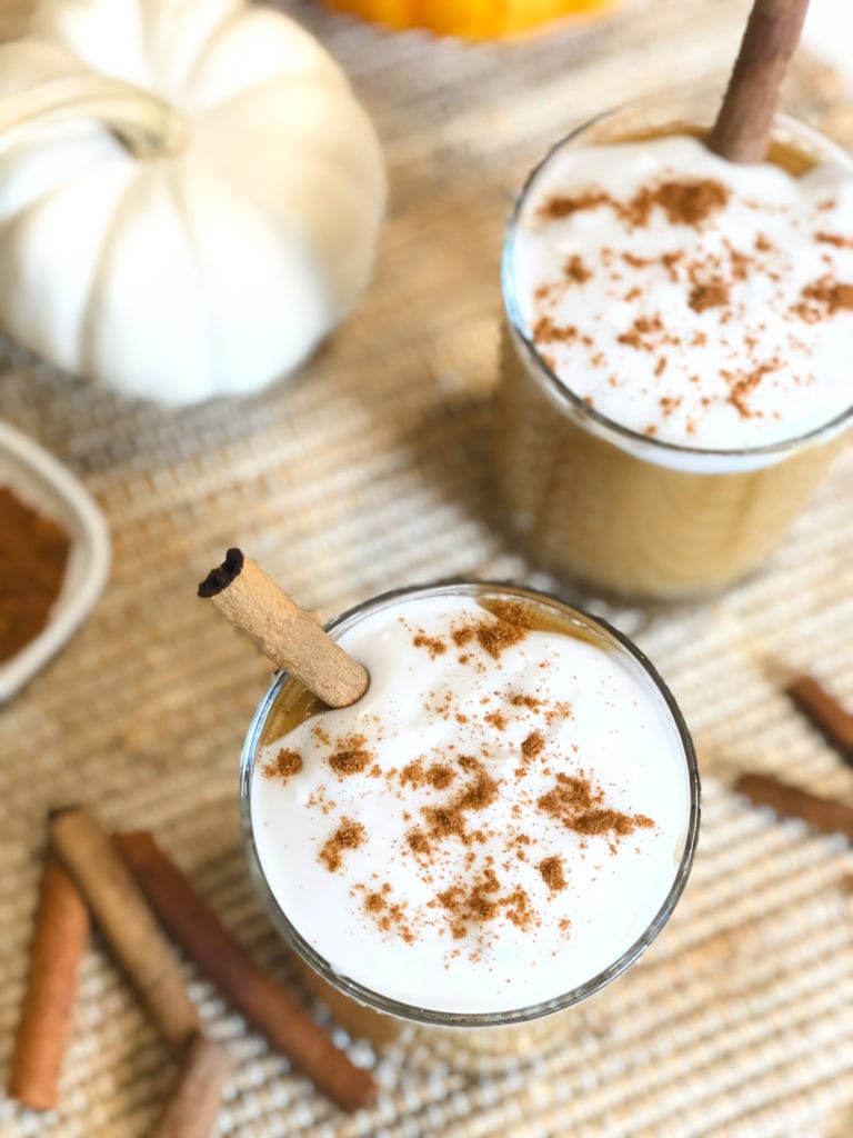 Close up of pumpkin pie smoothie in a glass with dairy free cream on top sprinkled with cinnamon.