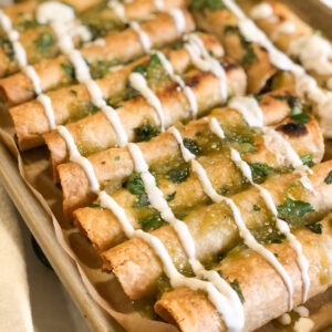 Close up of taquitos on sheet pan with salsa and cream sauce