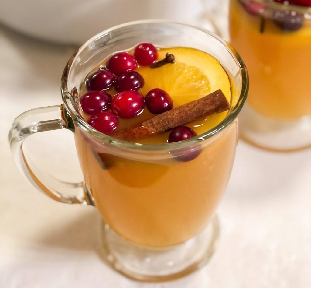 Homemade English Christmas Wassail in clear mug with cranberries and cinnamon stick.
